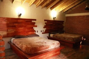 Un dormitorio con dos camas, cabeceros de madera, paredes de ladrillo y vigas de madera a la vista.