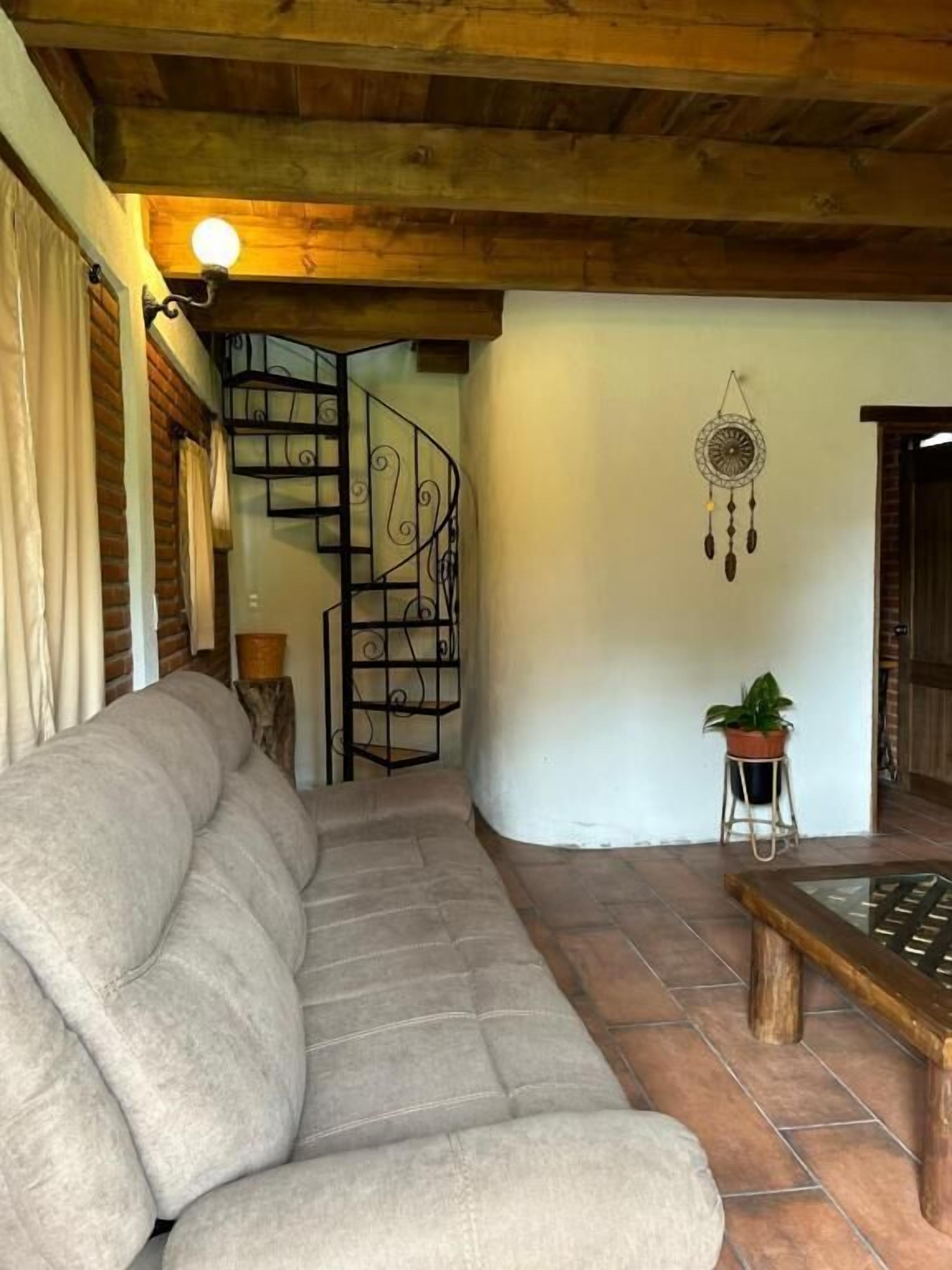 A living room with a sofa, a wooden coffee table, a spiral staircase, and a dreamcatcher on the wall.