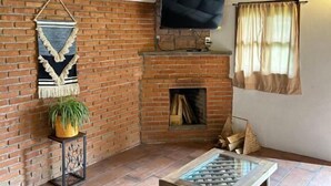 A rustic room with a brick fireplace, a television mounted above it, and a stone table in the center.