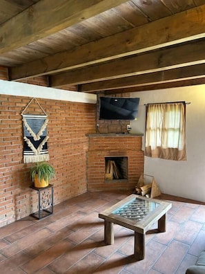 A rustic room with a brick fireplace, a television mounted above it, and a stone table in the center.