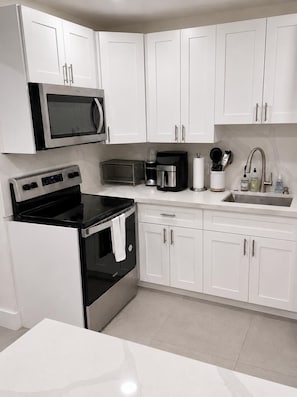 A modern kitchen with white cabinets, a microwave, a coffee maker, and a sink. - Bright, stylish 3BR/2BA pet-friendly retreat near Wynwood, Design District & MIA (Miami)