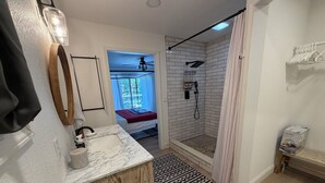 Une salle de bain avec une douche, un lavabo, un miroir et une fenêtre avec des rideaux.