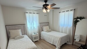 Une chambre avec deux lits, un ventilateur de plafond et une table de chevet avec une lampe.