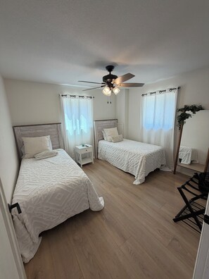 A bedroom with two beds, a ceiling fan, and a nightstand with a lamp. - Updated Lakefront Home in quiet cove makes the perfect swimming spot with a dock (Sunrise Beach)