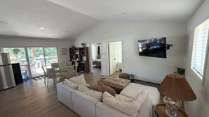 Un salon spacieux avec un grand canapé, un téléviseur fixé au mur et un coin repas comprenant des chaises et une table.