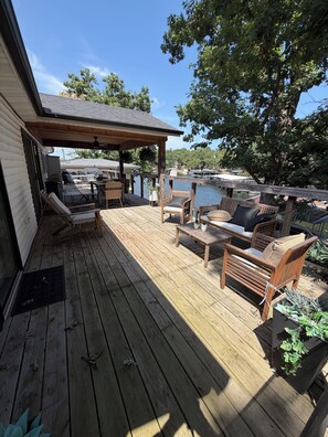 A wooden deck with outdoor furniture, a covered area, and a view of a body of water. - Updated Lakefront Home in quiet cove makes the perfect swimming spot with a dock (Sunrise Beach)