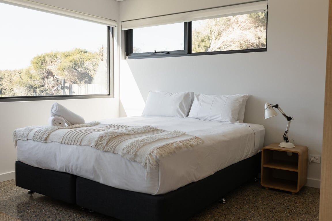 A bedroom with a bed, a nightstand, a lamp, and a window.