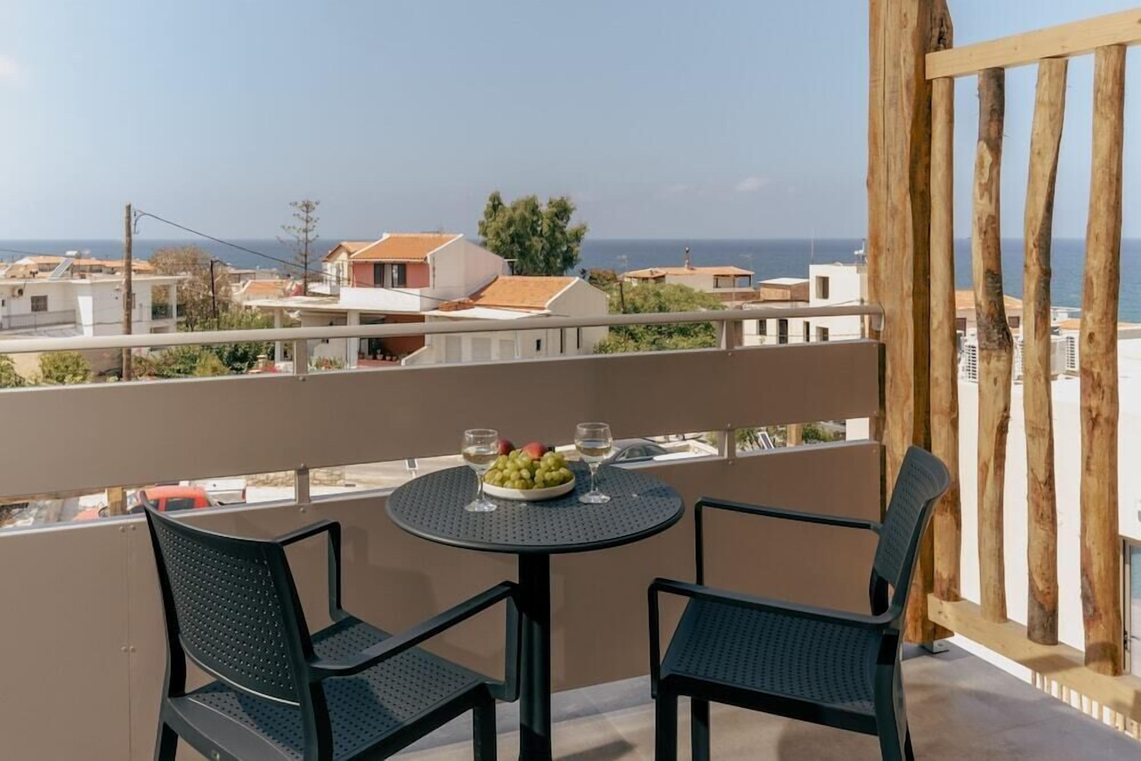 Un balcon avec une table ronde et deux chaises, un saladier rempli de fruits et deux verres de vin.