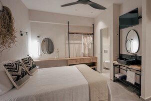 Un dormitorio moderno con cama, mesitas de noche, espejo, armario y baño con lavabo y espejo.