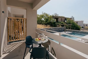 A balcony with a pool, a table with a plate of food, and chairs.