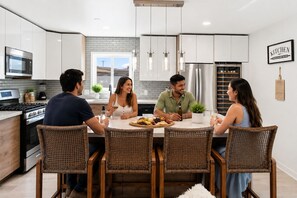 A modern kitchen with white cabinets, stainless steel appliances, and a dining area with wicker chairs. - Luxury 5BR Poway Home w/ Hot Tub, Hidden Room, Sleeps 12 (Poway)