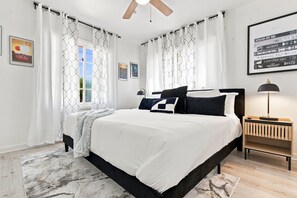 A bedroom with a bed, curtains, a nightstand, a lamp, and framed pictures on the wall. - Luxury 5BR Poway Home w/ Hot Tub, Hidden Room, Sleeps 12 (Poway)