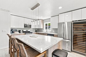 A modern kitchen with white cabinetry, a central island, stainless steel appliances, and a large window. - Luxury 5BR Poway Home w/ Hot Tub, Hidden Room, Sleeps 12 (Poway)