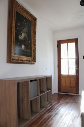 A room with a wooden floor, a door with glass panels, and a wall-mounted shelf with a framed picture.