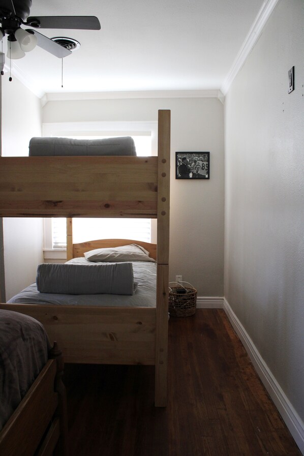 A bunk bed in a room with a ceiling fan, a framed photo on the wall, and a small basket on the floor.