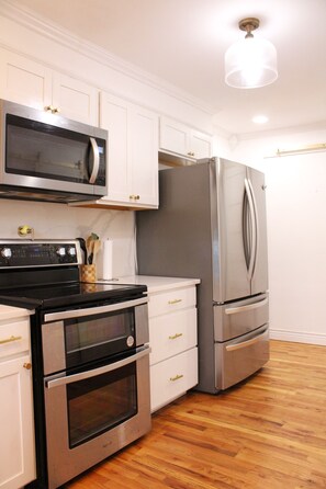A kitchen with stainless steel appliances, white cabinetry, and a wooden floor.