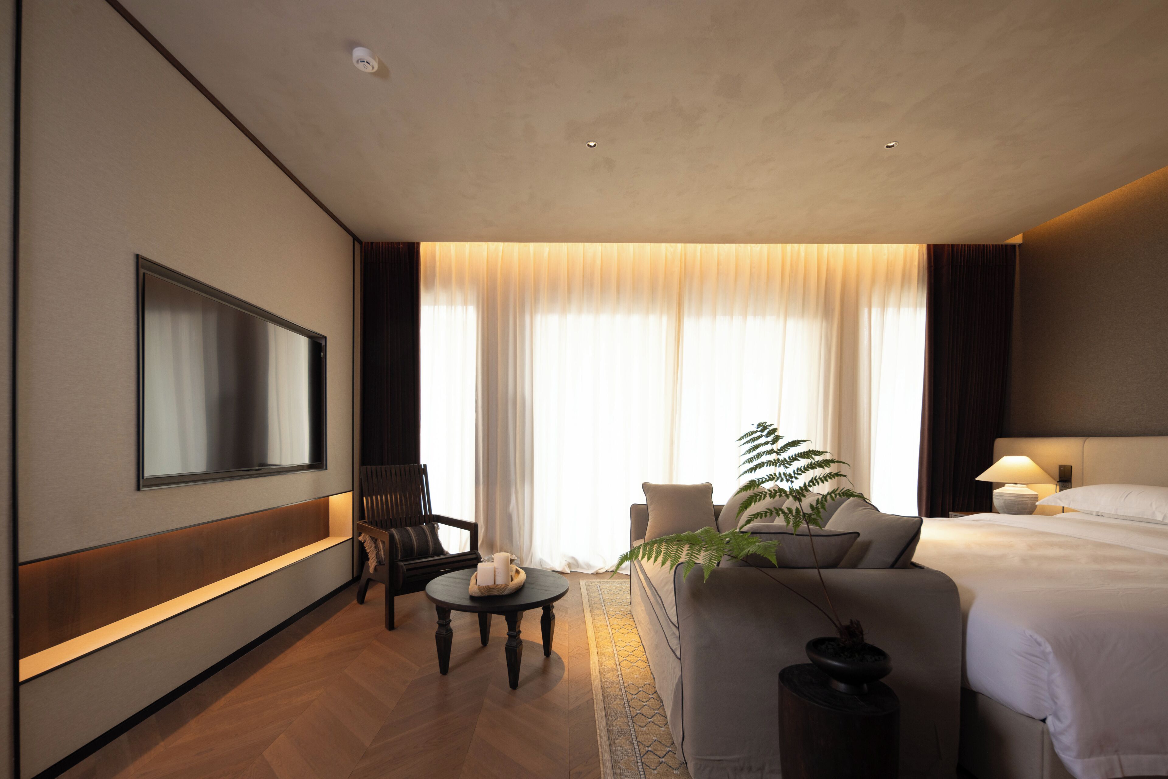 Een hotelkamer met een bed, een bank, een televisie, een tafel met kaarsen en een plant.