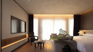 Una habitación de hotel con cama, sofá, televisión, una mesa con velas y una planta.