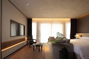 Een hotelkamer met een bed, een bank, een televisie, een tafel met kaarsen en een plant.