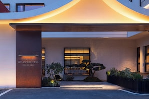 Entrada de hotel con diseño moderno, un toldo grande iluminado y un cartel.