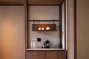 Een kitchenette met een houten plank waarop een theepot, bekers, een koffiezetapparaat en waterflessen staan.