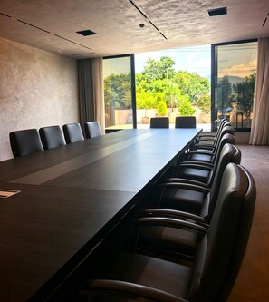 A conference room with a long table and chairs, large windows with a view of greenery, and a modern ceiling design.