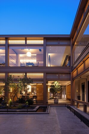 A modern building with a glass facade, outdoor seating area, and a well-lit interior.