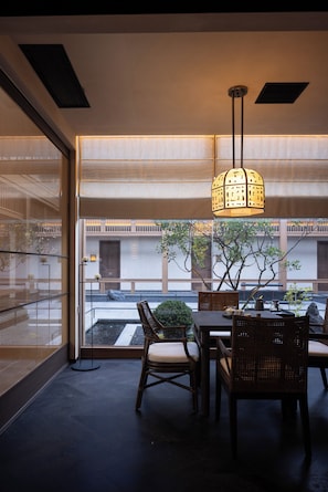 Un comedor interior con una mesa, sillas, una lámpara colgante y vistas al exterior.