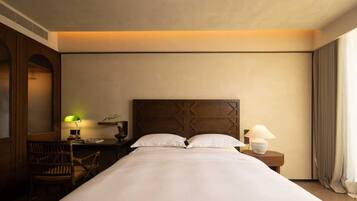 A hotel room with a large bed, a wooden headboard, a nightstand with a lamp, a chair, and a window with curtains.