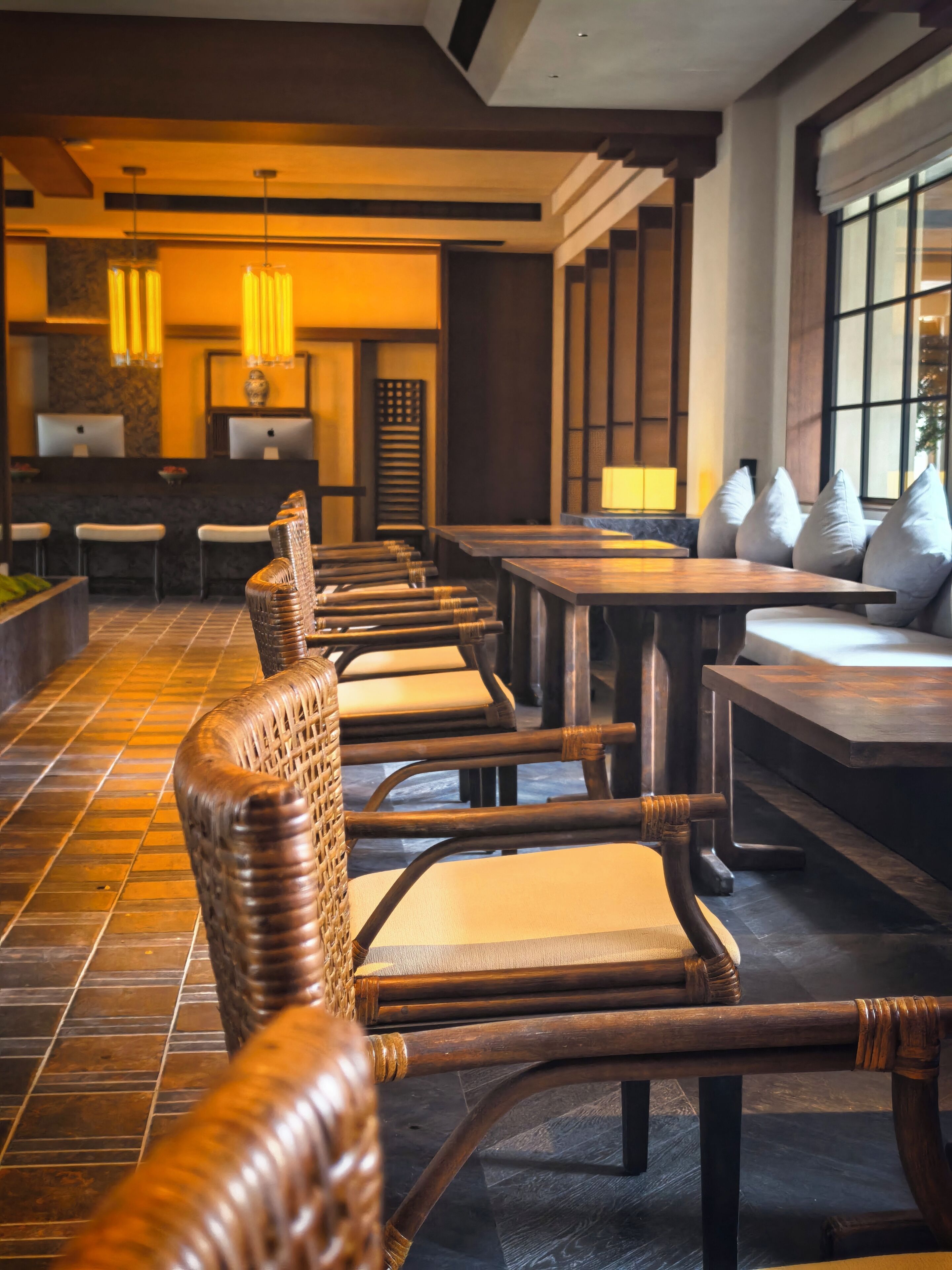 Un hall de hotel con mostrador de recepción, zona de estar con sillas y mesas, y piso de baldosas.