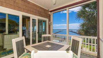 A covered outdoor area with a table and chairs, a view of the water, and a wooden deck.