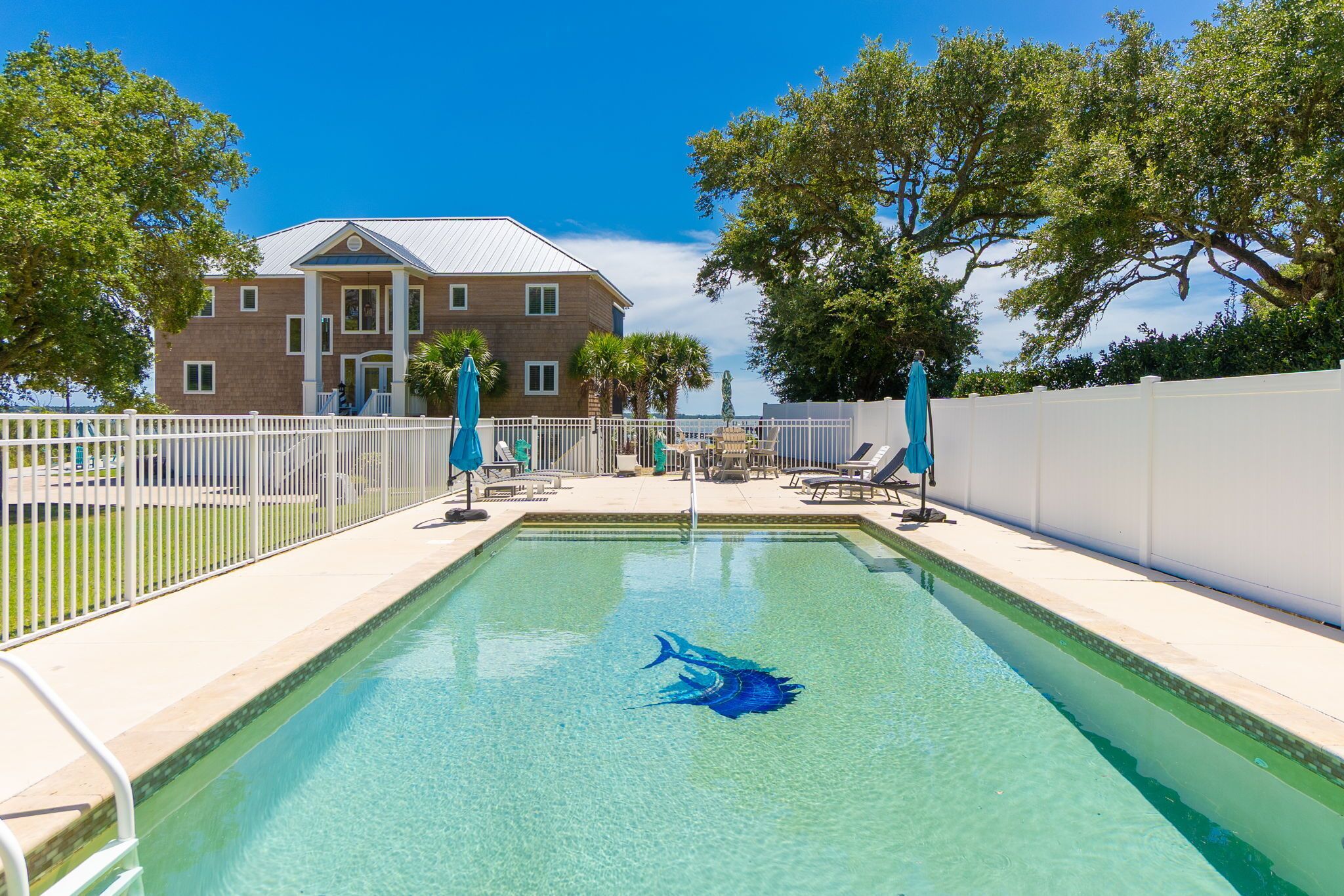 Una piscina con una decoración de cangrejo, rodeada por una valla blanca, con un edificio y árboles al fondo.