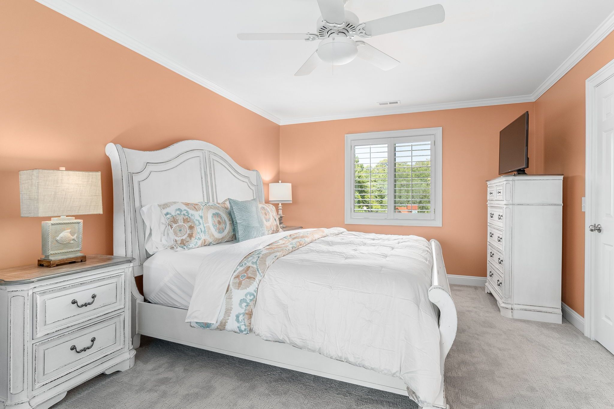 A bedroom with a bed, nightstands, a dresser, a ceiling fan, and a window with blinds.