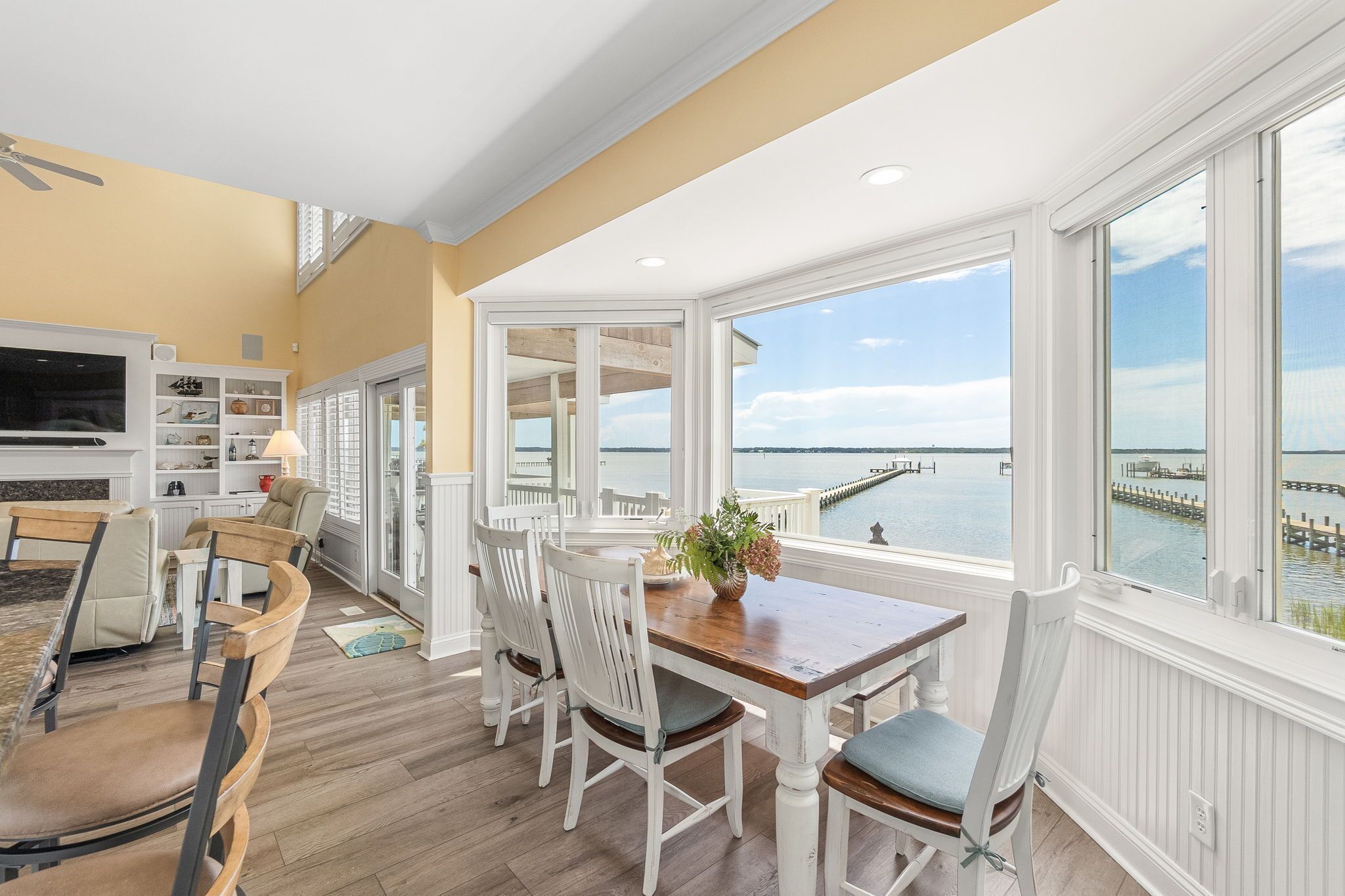 A dining area with a view of the water, wooden flooring, and white furniture.