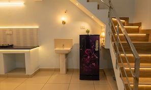 A modern kitchen with a built-in sink, a refrigerator with a floral design, and a staircase with wooden steps. - Urban white Villa Homestay with 2-bedroom AC in charming Puducherry (Puducherry)