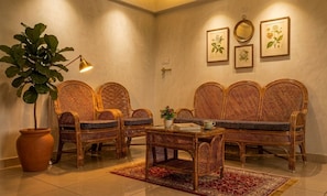 A room with wicker furniture, a potted plant, and framed botanical prints on the wall.