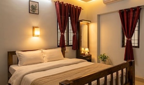 A bedroom with a bed, a nightstand with a lamp, a mirror, and red curtains. - Urban white Villa Homestay with 2-bedroom AC in charming Puducherry (Puducherry)