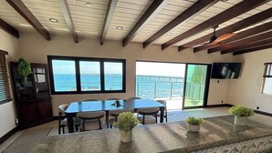 A kitchen with a large island, dining table, and chairs, with a view of the ocean and a bridge. - Oceanfront - Island Views - Shoals Beach House (Ventura)