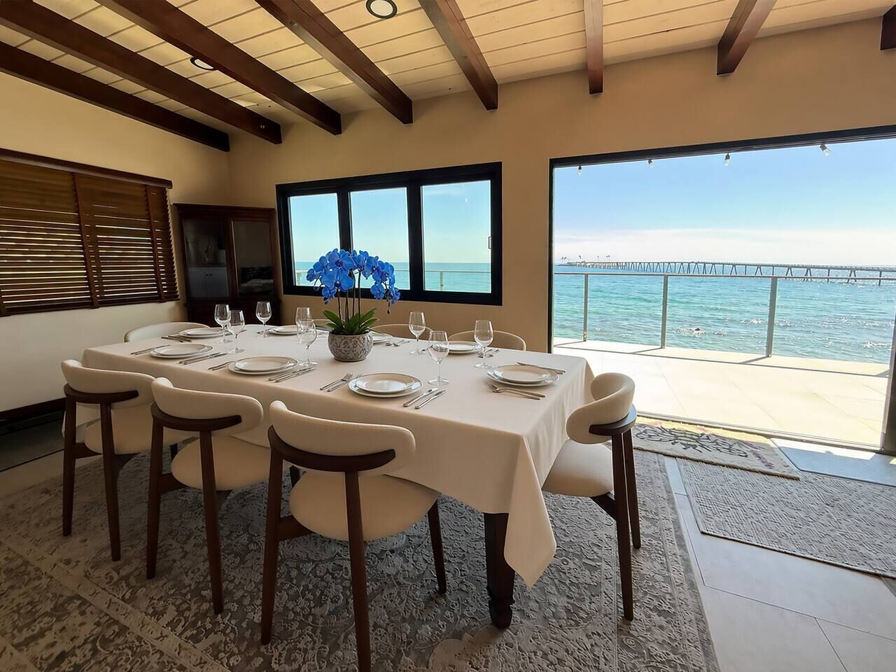 A dining area with a table set for six, overlooking a body of water and a pier.