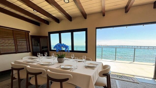 A dining area with a table set for six, overlooking a body of water and a pier. - Oceanfront - Island Views - Shoals Beach House (Ventura)