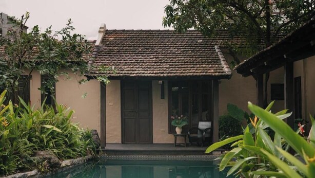 Um edifício tradicional com telhado de azulejos, piscina e vegetação exuberante.
