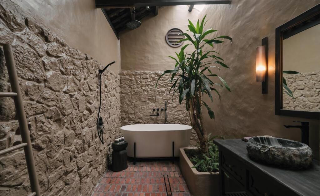 A bathroom with a stone wall, a bathtub, a potted plant, and a mirror.