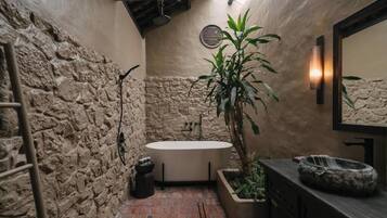 A bathroom with a stone wall, a bathtub, a potted plant, and a mirror.