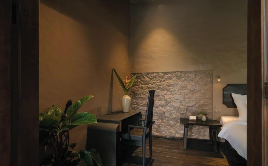 A room with a bed, a small table, a chair, and a potted plant.