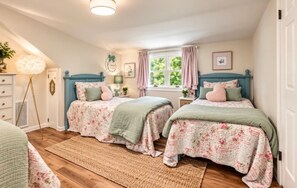 A bedroom with two beds, a bedside table, a lamp, a window with curtains, and a floor lamp.