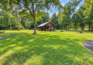 A rustic wooden cabin with a porch, surrounded by a well-maintained lawn and tall trees.