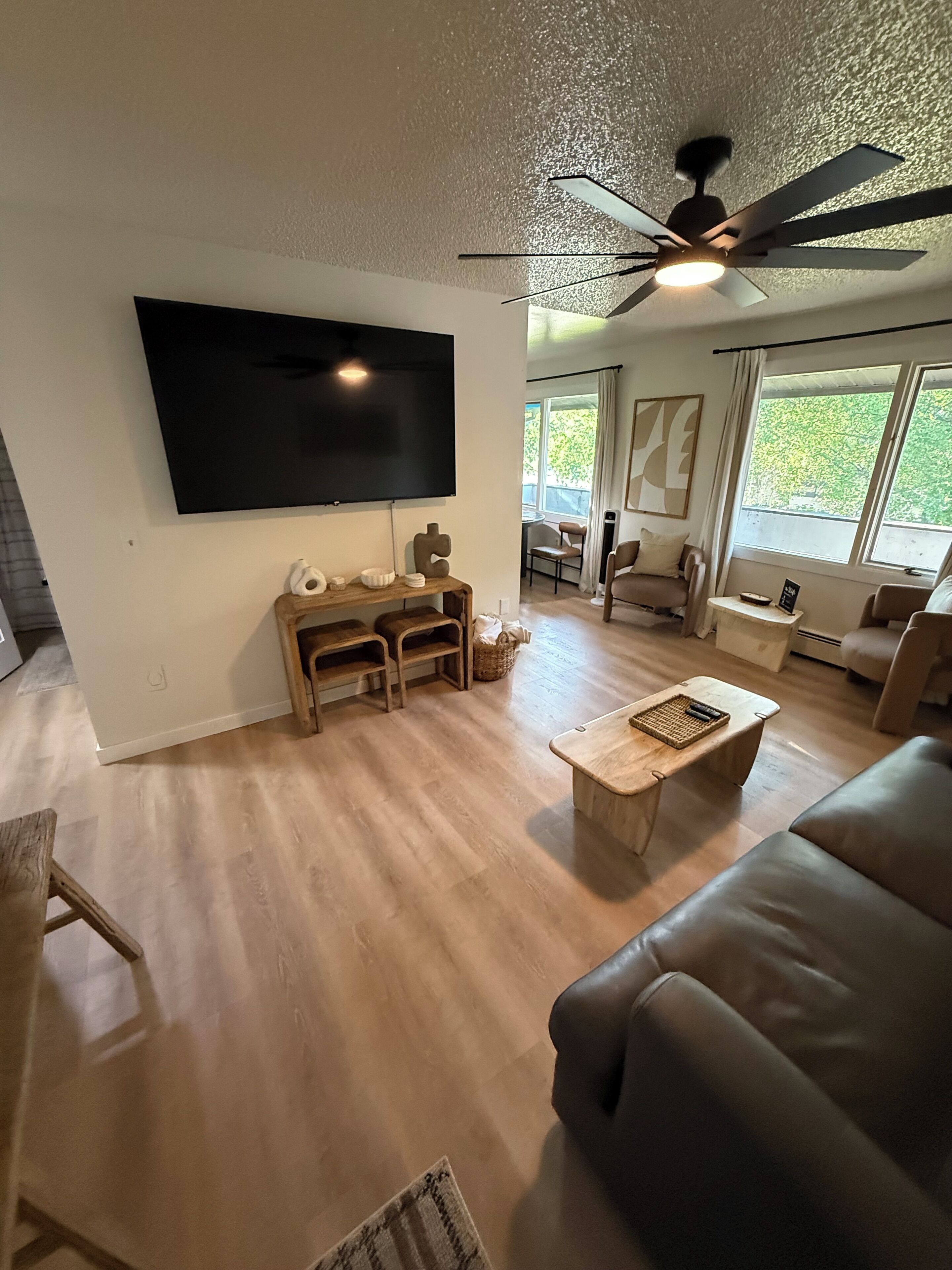 Un salon doté d’un téléviseur à écran plat, de meubles en bois, d’un ventilateur de plafond et de grandes fenêtres.