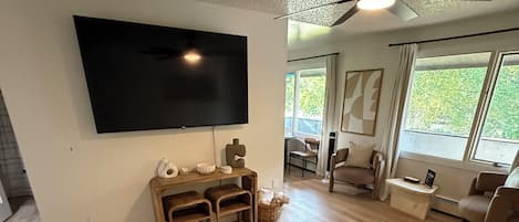 Un salon doté d’un téléviseur à écran plat, de meubles en bois, d’un ventilateur de plafond et de grandes fenêtres.