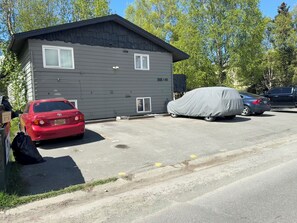 Ein zweistöckiges Gebäude mit Garage, ein rotes Auto vor der Tür und ein überdachtes Auto auf der Auffahrt.