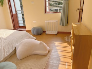 Un dormitorio con cama, cómoda de madera, ventana con cortinas, radiador y un taburete pequeño.